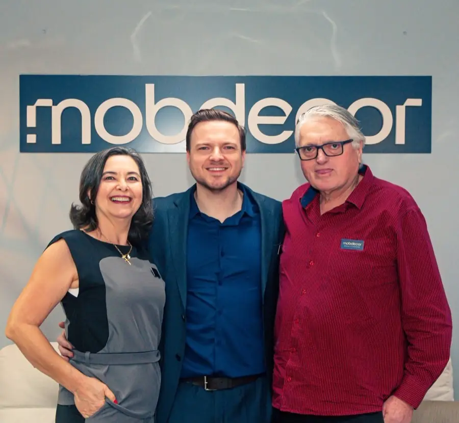 Renan Lunardelli entre os pais, os três sorrindo na loja, sob o letreiro da Mobdecor
