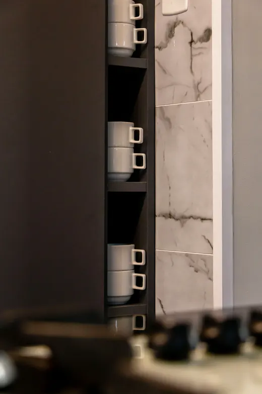 Detalhe de nicho vertical em armário grafite, com prateleiras de xícaras junto ao revestimento de mármore